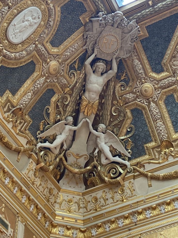 an ornately decorated ceiling with gold and white decorations on it's sides, including two cherubs