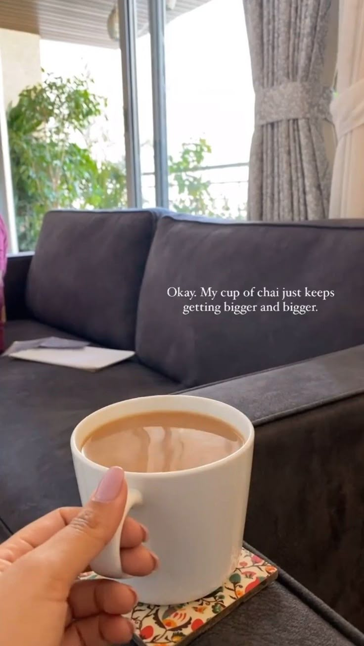 a person holding a cup of coffee on top of a table next to a couch