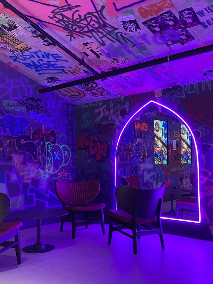 a room with graffiti all over the walls and purple lighting on the ceiling, along with chairs