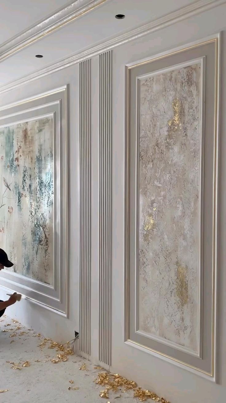 a man kneeling down to paint a wall with gold flakes on the floor next to it