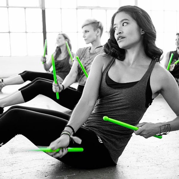 a group of people sitting on the floor with green sticks in their hands and one person standing behind them