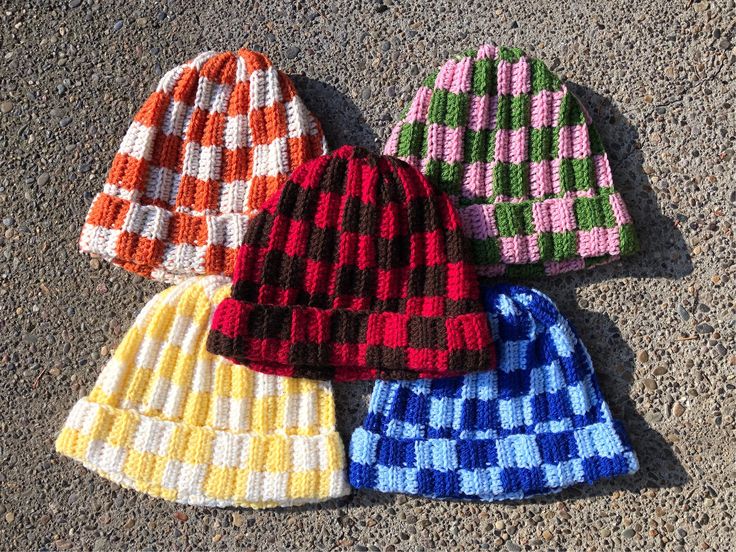 three knitted hats laying on the ground next to each other, all in different colors