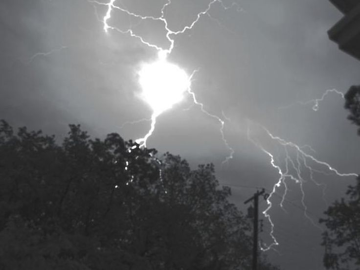 the sun is shining through some clouds with lightning striking over it in this black and white photo