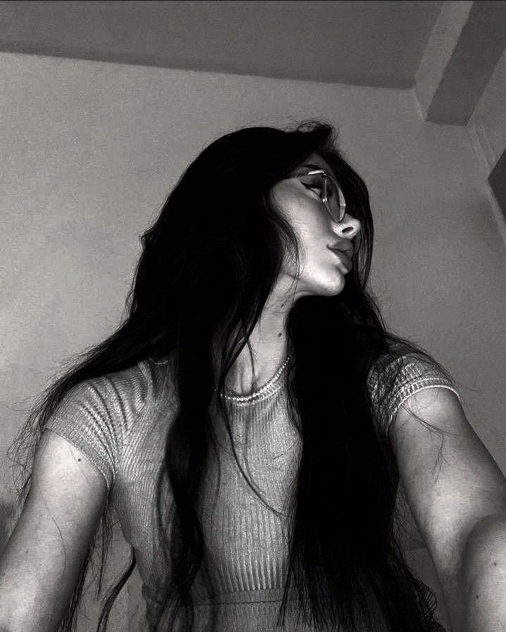 a black and white photo of a woman with long dark hair wearing glasses looking off into the distance