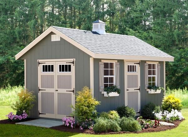 a small gray shed with windows and flowers in the front yard