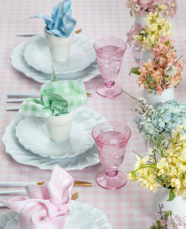 the table is set with pink and white dishes, napkins, and vases