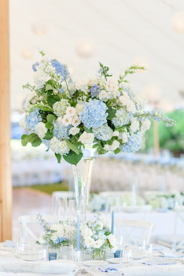 a vase filled with blue and white flowers on top of a table covered in glasses