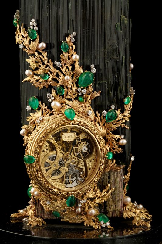 a gold clock with green and white jewels on it's face, sitting next to a black background