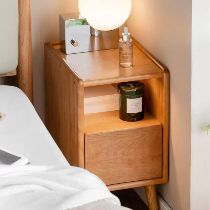 a wooden night stand with a lamp on top of it next to a white bed