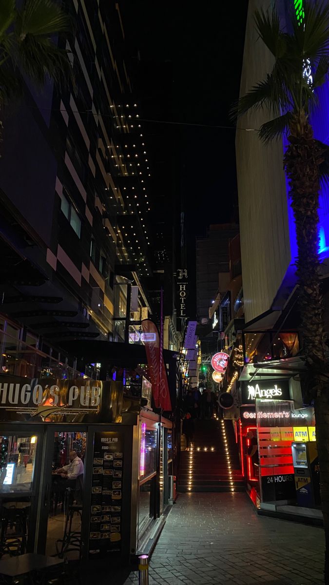 a city street at night with palm trees and neon signs on the side of buildings