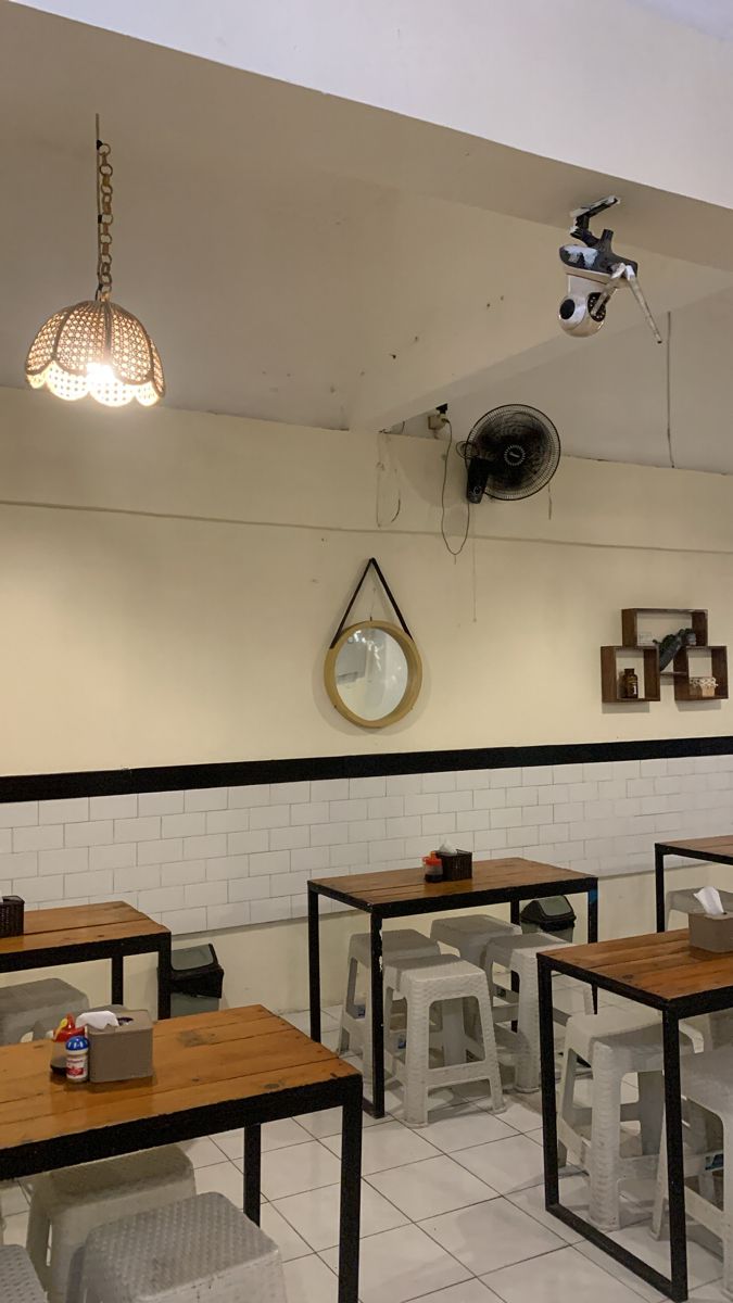 an empty restaurant with wooden tables and white tile flooring, hanging lights and round mirrors