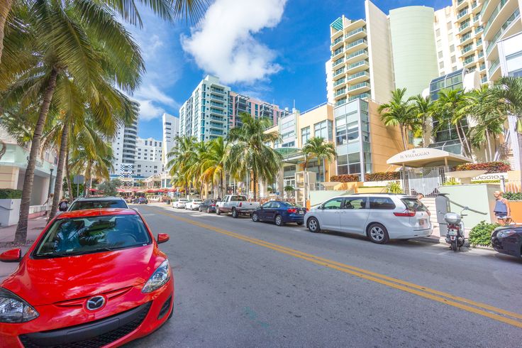 a red car parked on the side of a road next to tall buildings and palm trees