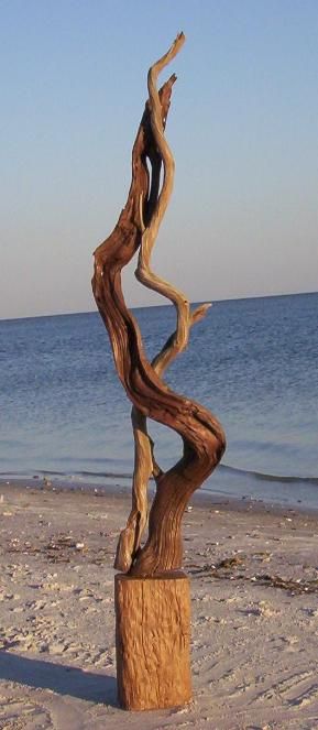 a wooden sculpture on the beach with water in the background