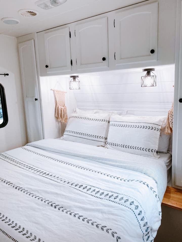 a bed with white linens and pillows in a small room next to some cupboards