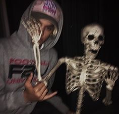 a man in a hoodie is holding a fake skeleton and pointing it at the camera