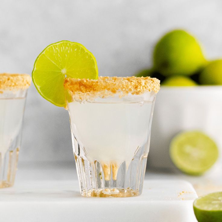 two margaritas with lime and sugar on the rim, one garnished with a lime