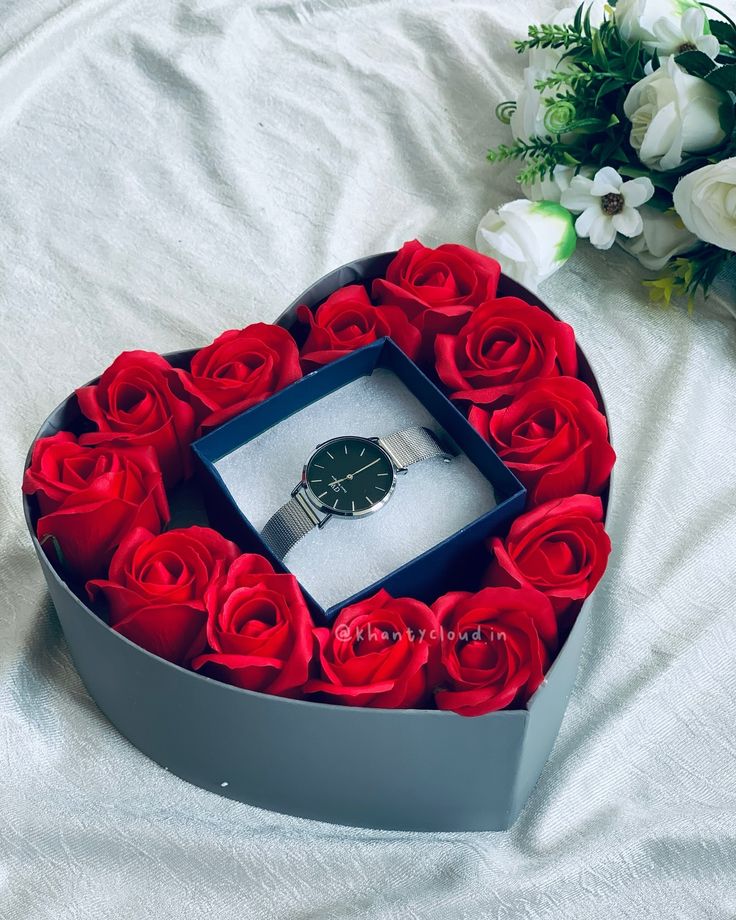 a heart shaped box filled with red roses and a watch sitting on top of it