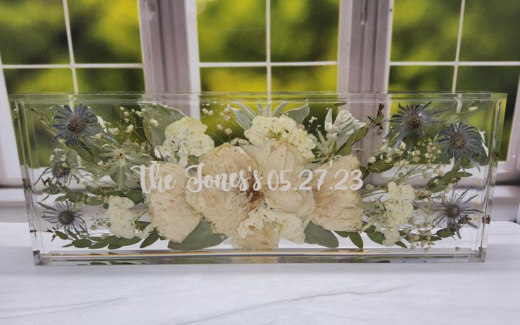 a clear acrylic box with flowers and greenery in front of a window