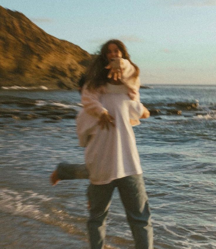 a woman walking on the beach with her dog in her arms and she's holding an animal