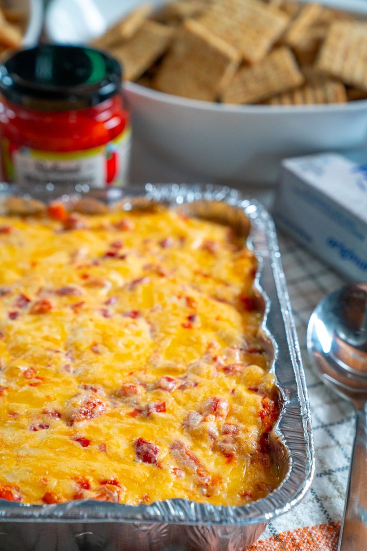 a cheesy casserole in a pan with some crackers on the side