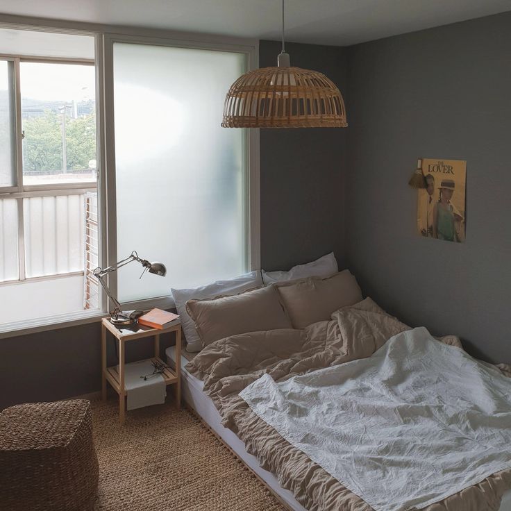 an unmade bed sitting next to a window with a lamp hanging over the headboard