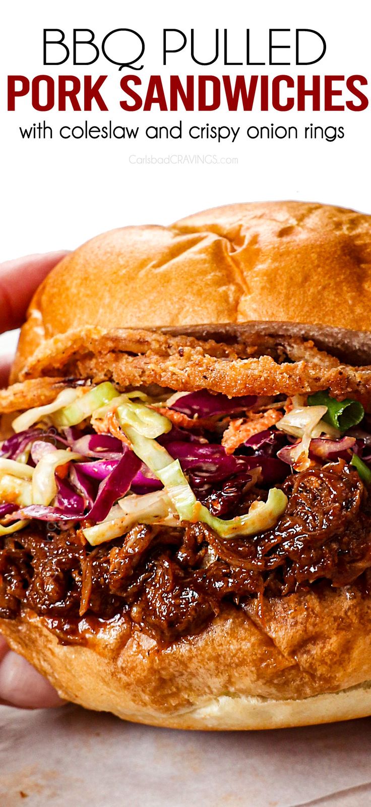 a hand holding a pulled pork sandwich with coleslaw and crispy onion rings