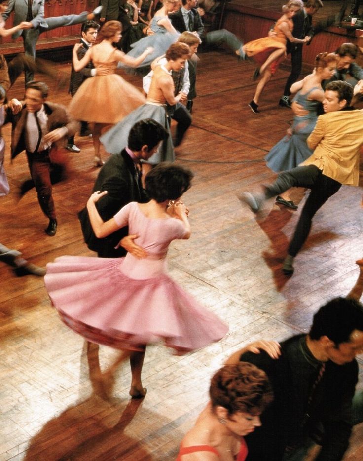 a group of people dancing on a wooden floor in a dance hall with other people