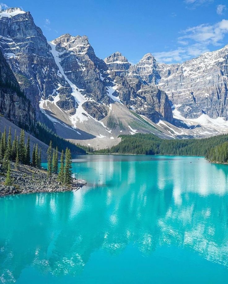 a lake surrounded by mountains and trees in the middle of it's blue waters