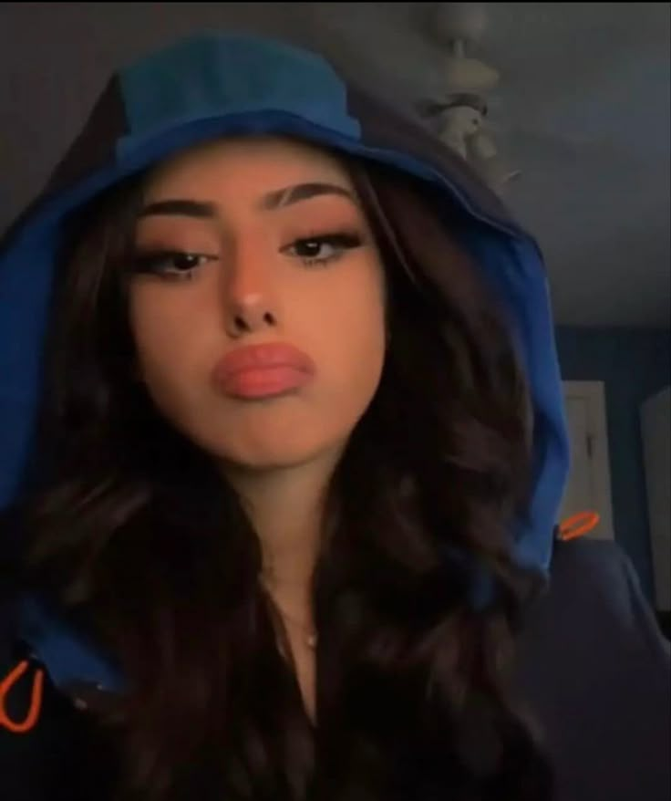 a woman with long hair wearing a blue hoodie and looking at the camera while making a funny face