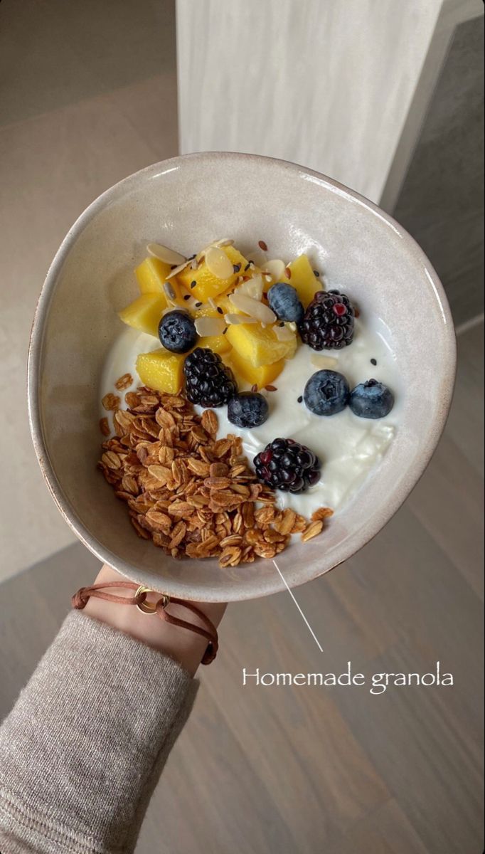 a person holding up a bowl of cereal with yogurt, fruit and granola