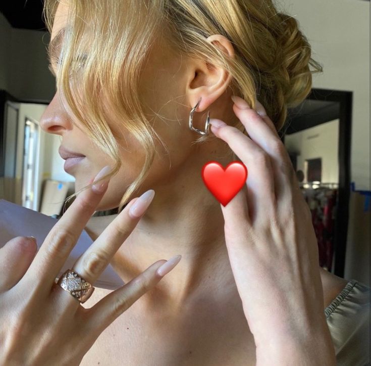 a woman with blonde hair and red heart shaped earrings on her ear is looking into the mirror