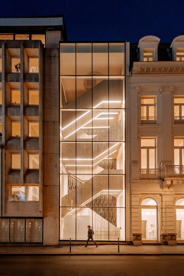 a person walking in front of a building at night with lights on the windows and stairs lit up