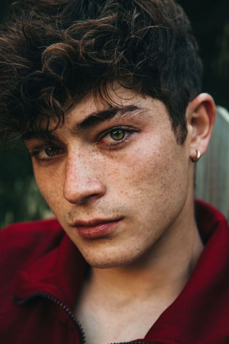 a young man with freckled hair and piercings looks at the camera while wearing a red shirt