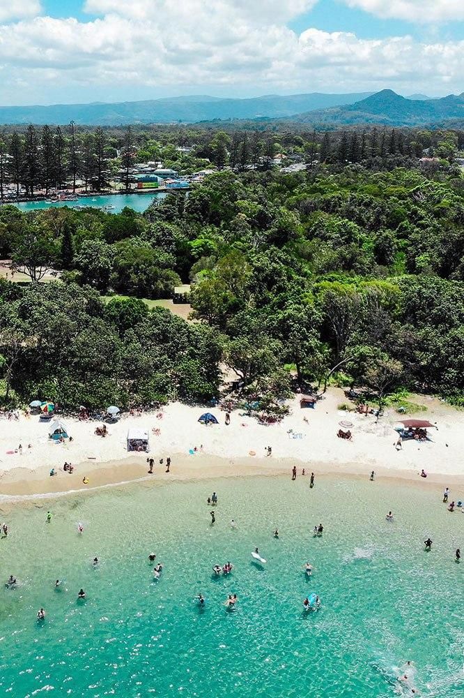 an aerial view of people on the beach and in the water, surrounded by trees