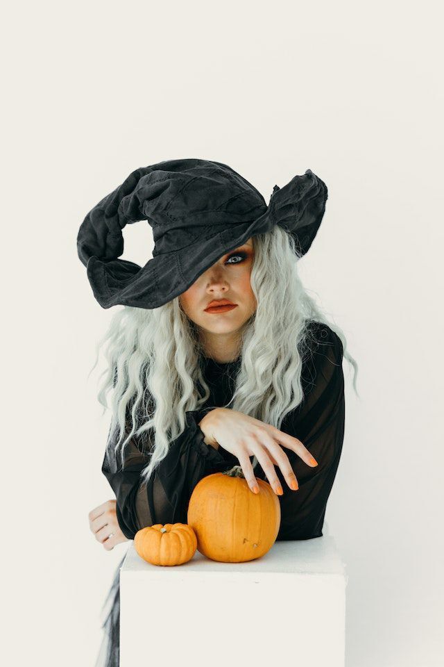 a woman with long white hair wearing a black hat and holding a small orange pumpkin