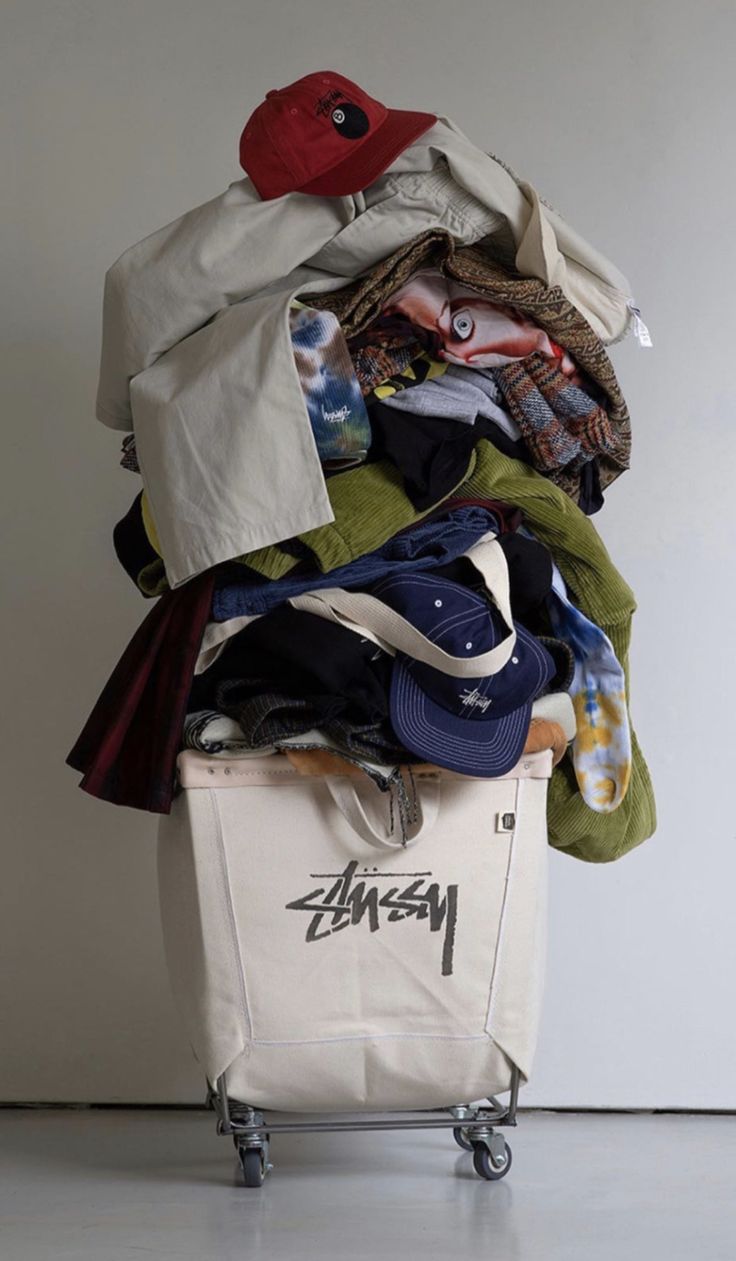 a pile of clothes sitting on top of a white suitcase next to a wall with a red hat