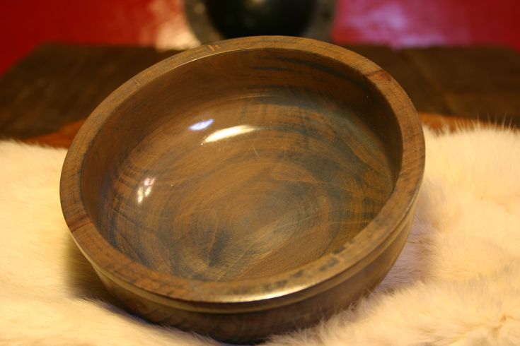 a wooden bowl sitting on top of a white fur covered floor next to a black vase