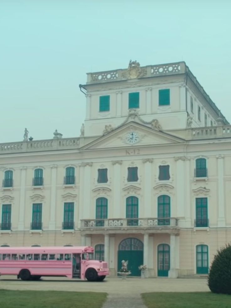 two pink buses are parked in front of a large white building with green shutters