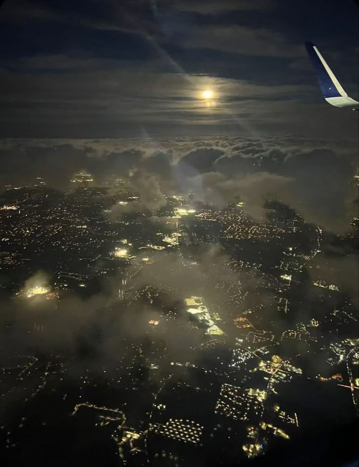 an airplane wing flying over the city lights and clouds at night in the dark sky