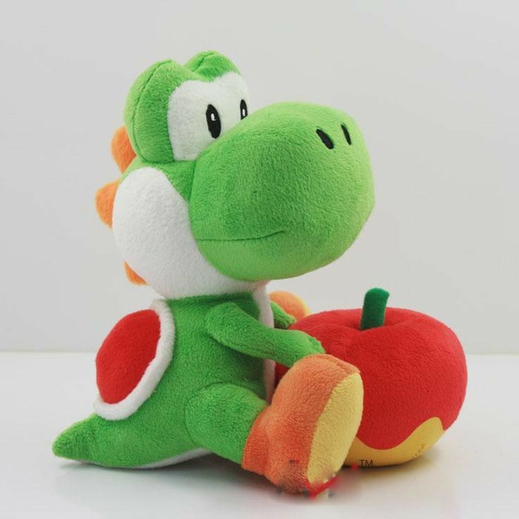 a green stuffed animal sitting on top of a white table next to a red apple