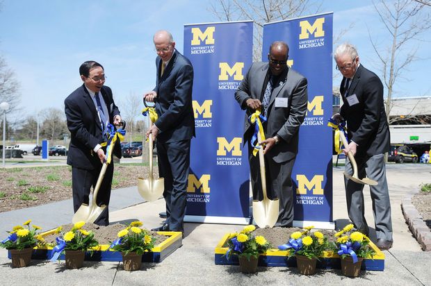 four men are holding shovels and digging in the ground with flowers on them while another man stands behind them