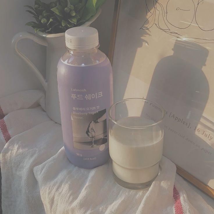 a bottle of liquid next to a glass on a towel with a potted plant in the background