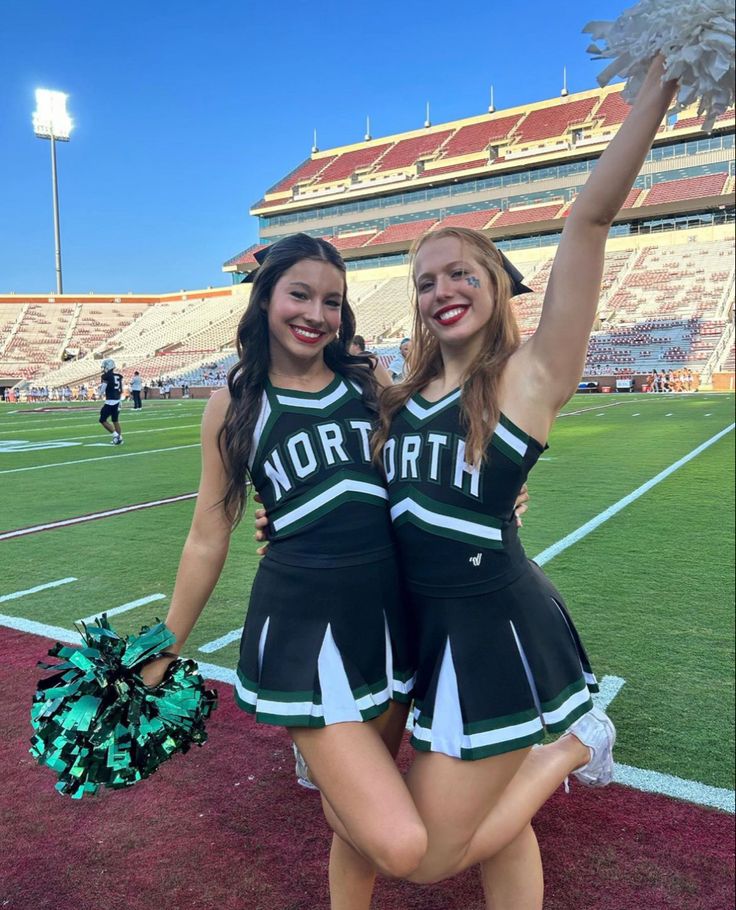 two cheerleaders pose for the camera at a football game