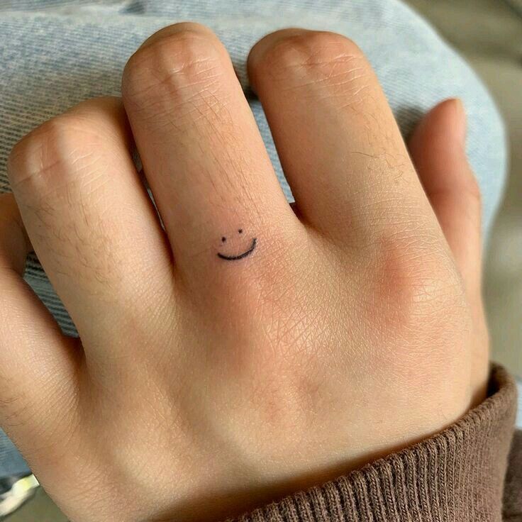 a person's hand with a small smiley face tattoo on their left ring finger