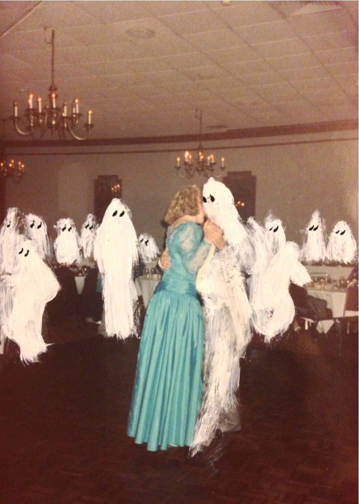 a woman in a blue dress is surrounded by ghost figurines and chandeliers