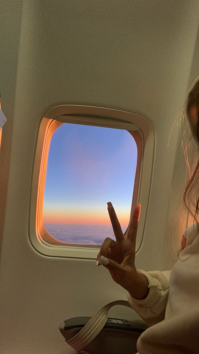 a woman sitting on an airplane with her hand up in the air while looking out the window