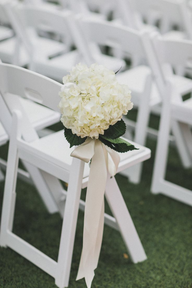 a bouquet of white hydrangeas tied to the back of an outdoor ceremony chair