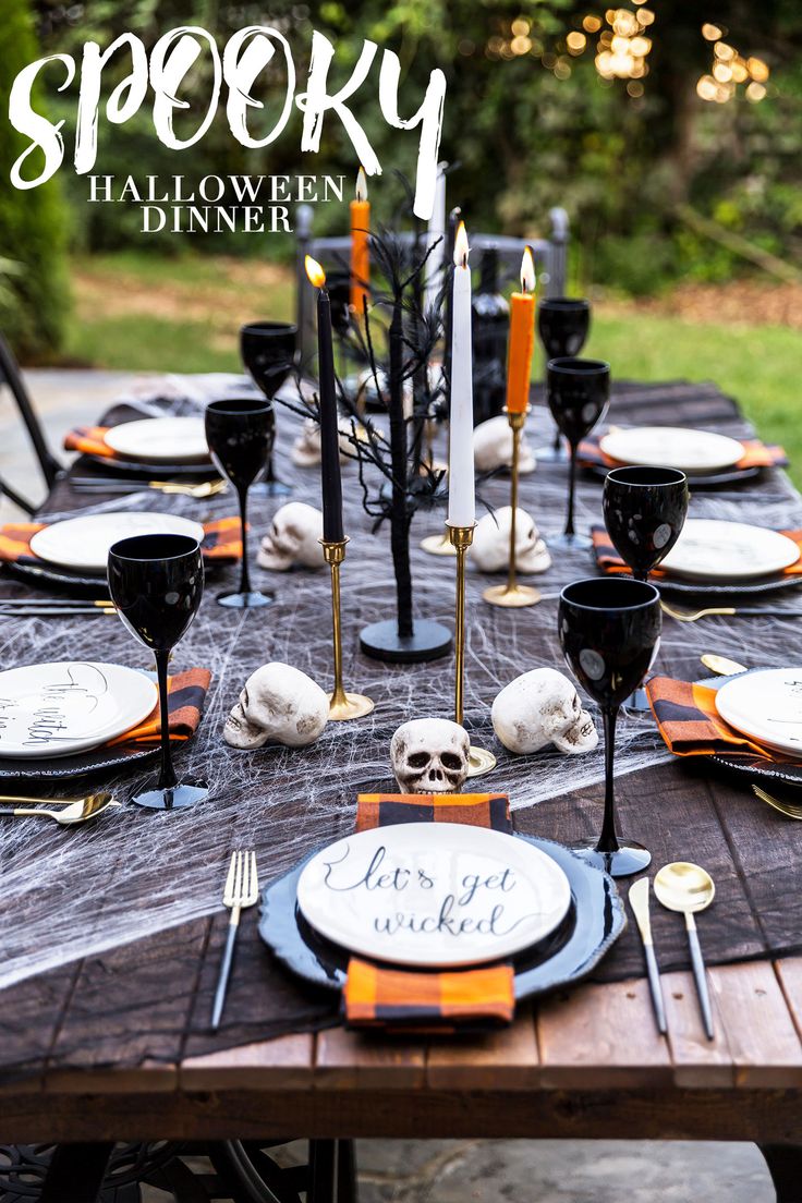 an outdoor table set for halloween dinner with black and white plates, silverware and candles