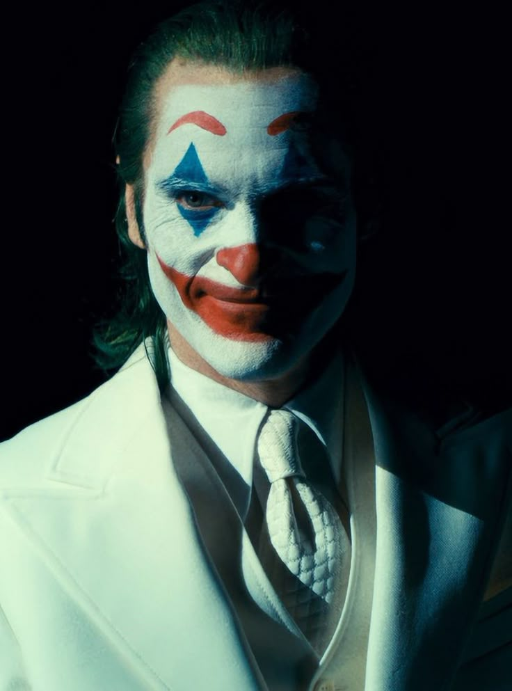 a man in a white suit and clown makeup is posing for the camera with his face painted red, white and blue