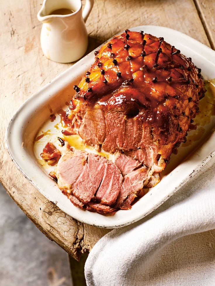 a roast beef covered in barbecue sauce on a white platter next to a cup of coffee